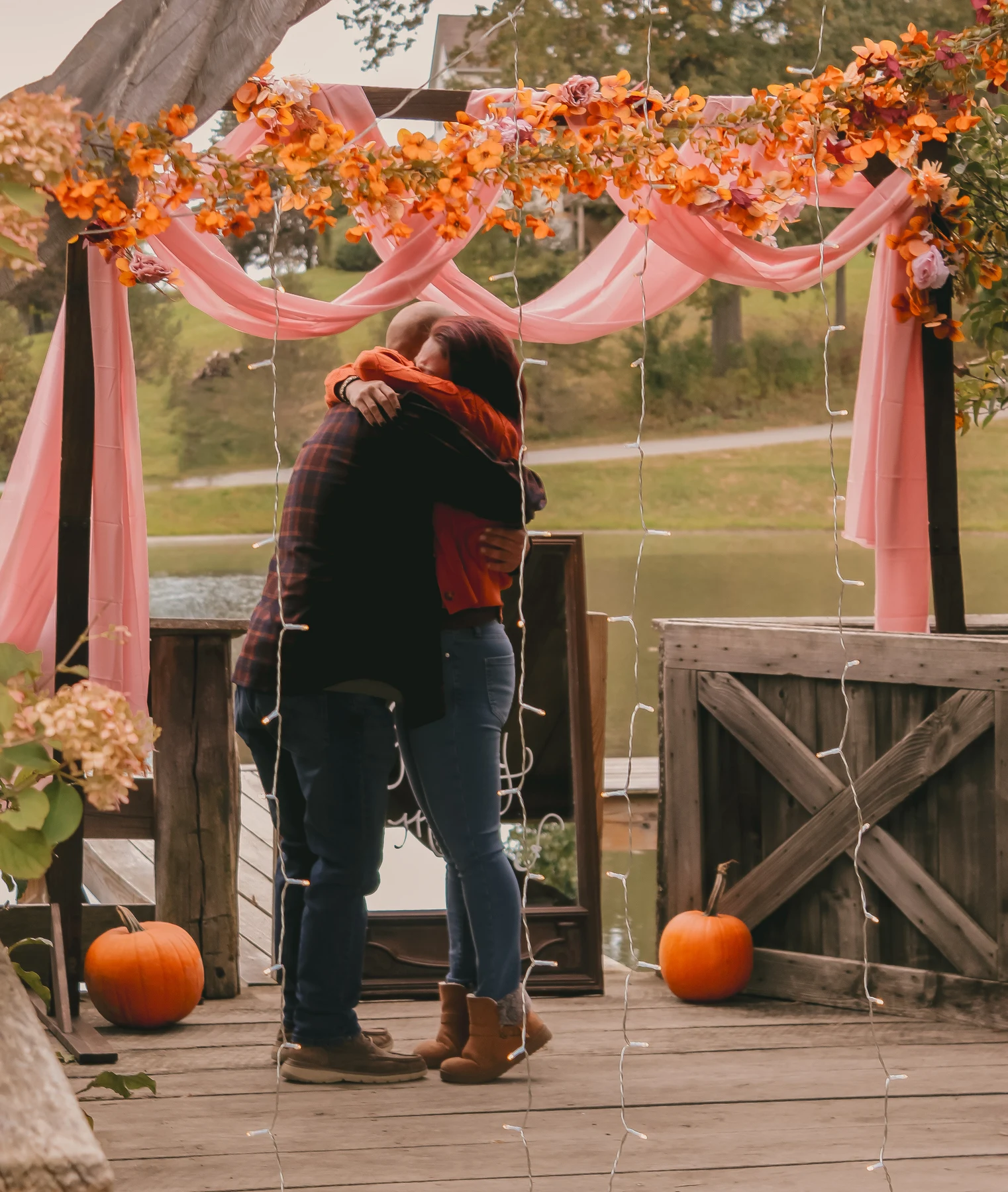 Couple embracing beneath a floral arch with pink drapery and pumpkins