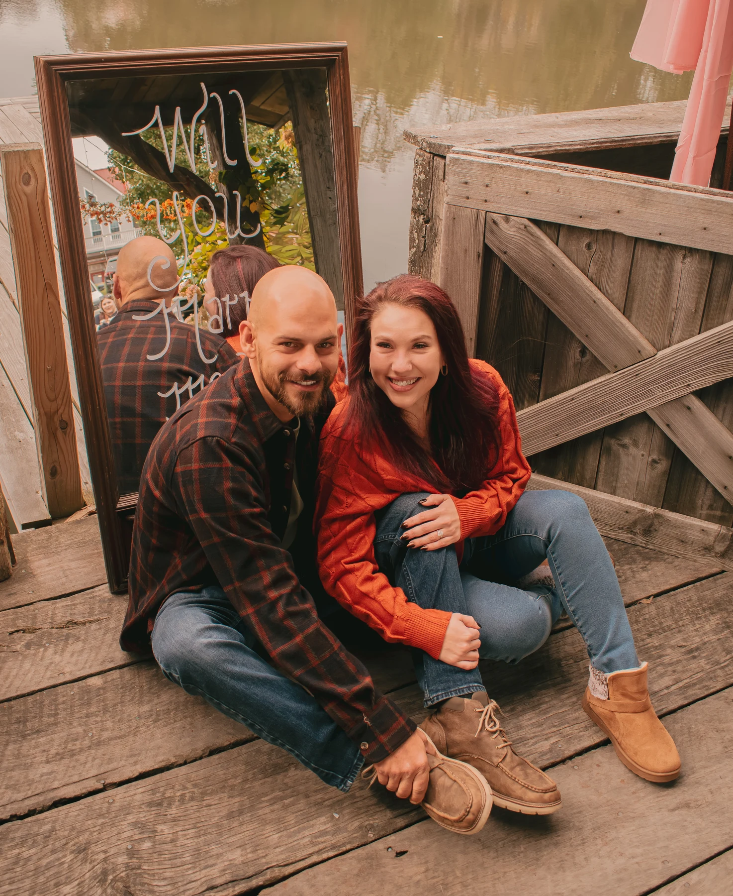 Engaged couple smiling together on a wooden deck beside the proposal mirror