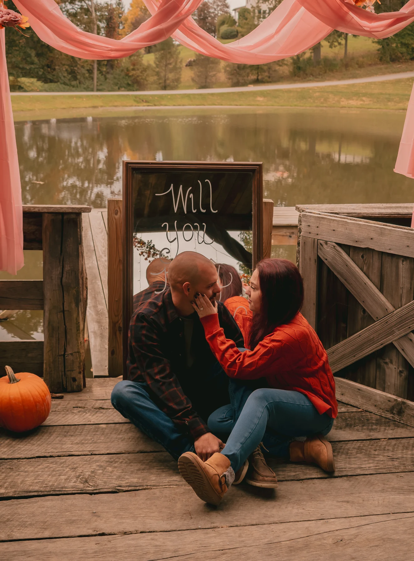 Couple seated together beneath pink drapery, sharing a quiet moment beside the pond