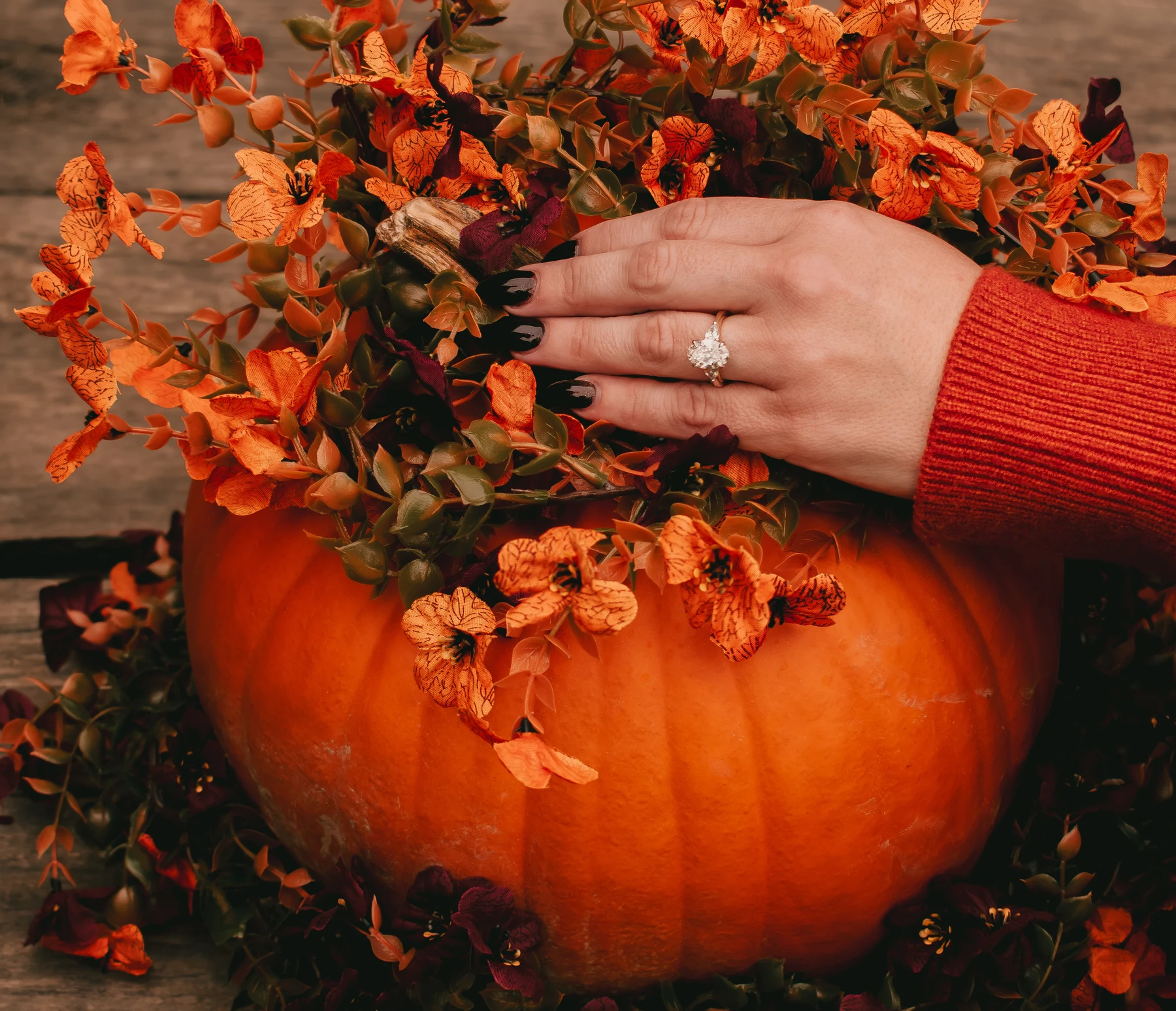 Engagement ring on a hand resting among autumn flowers over a pumpkin