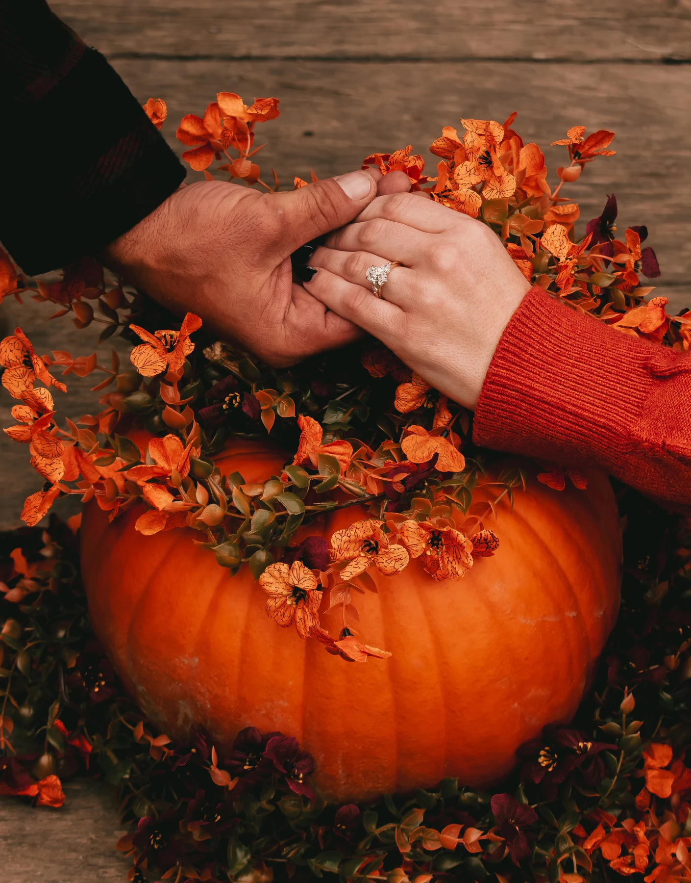 Joined hands and an engagement ring above a pumpkin and autumn flowers