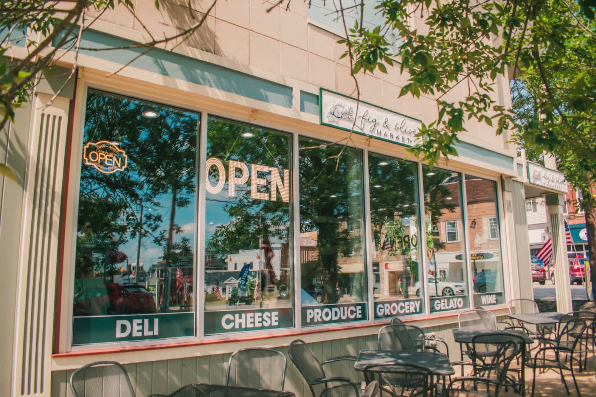 Sunlit specialty market storefront with window lettering for deli, cheese, produce, grocery, and gelato