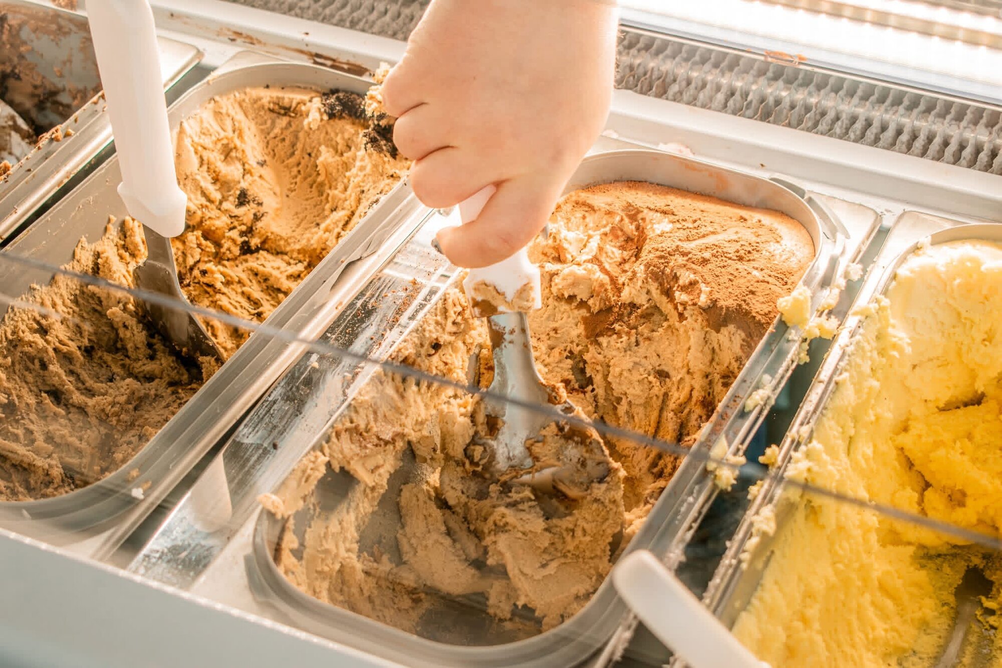 Close-up of gelato being scooped from trays in a display case
