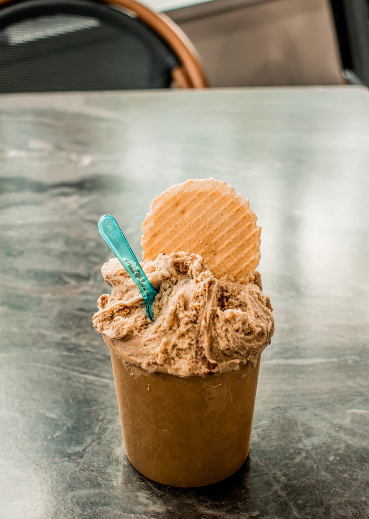 Cup of gelato with a waffle cookie and spoon on a marble cafe table