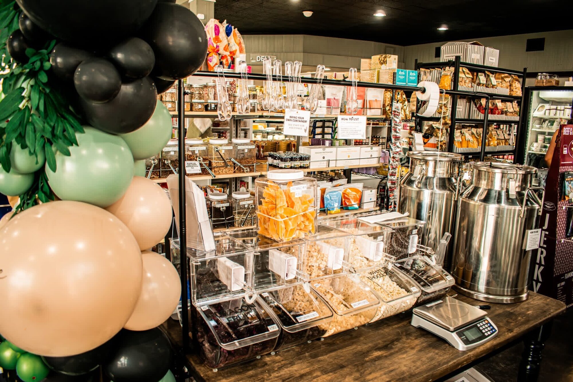 Bulk foods section with dispensers, milk cans, and a weigh scale