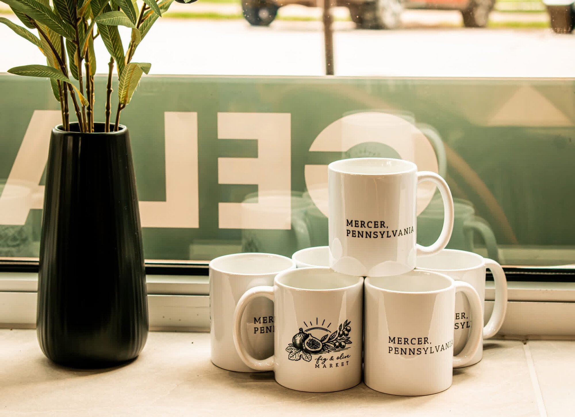 Stacked ceramic mugs with Mercer, Pennsylvania branding styled in a shop window