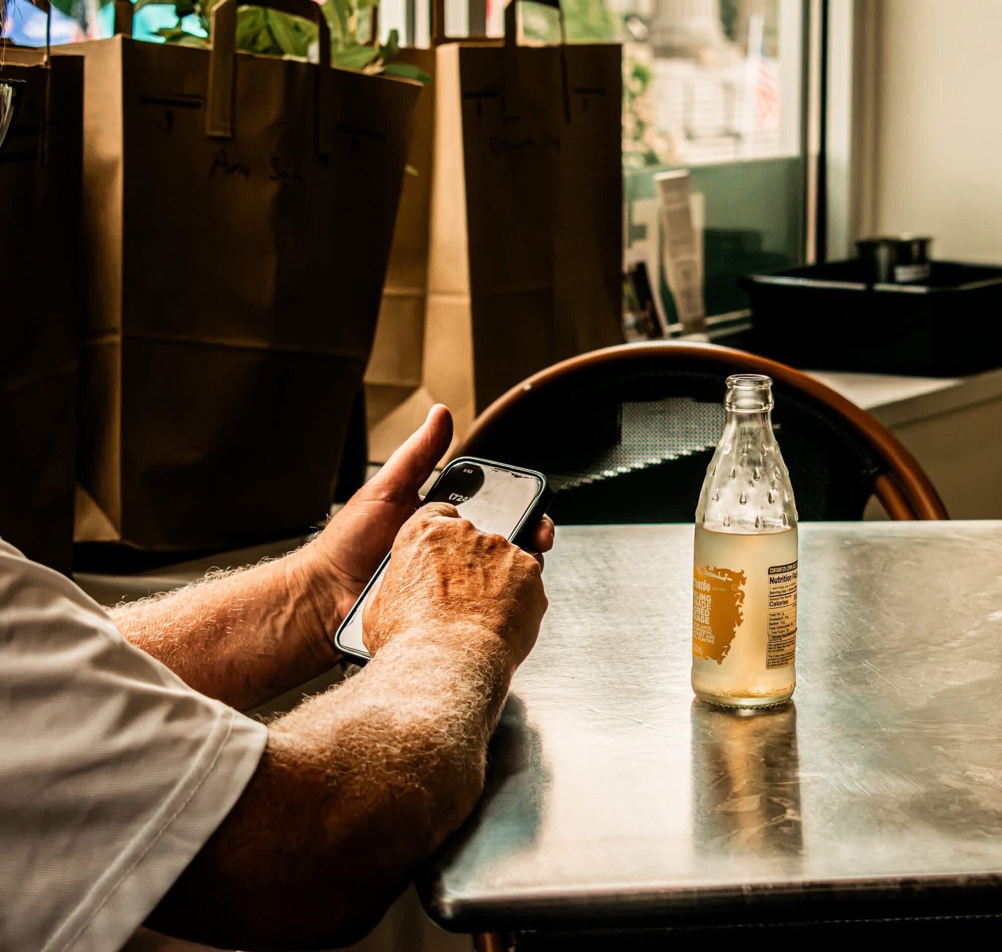 Customer at a cafe table with a bottled drink and phone, candid lifestyle shot