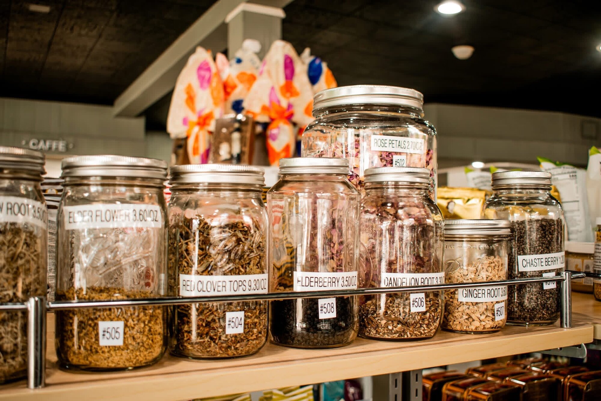 Glass apothecary jars of loose-leaf herbs and botanicals on a wooden shelf