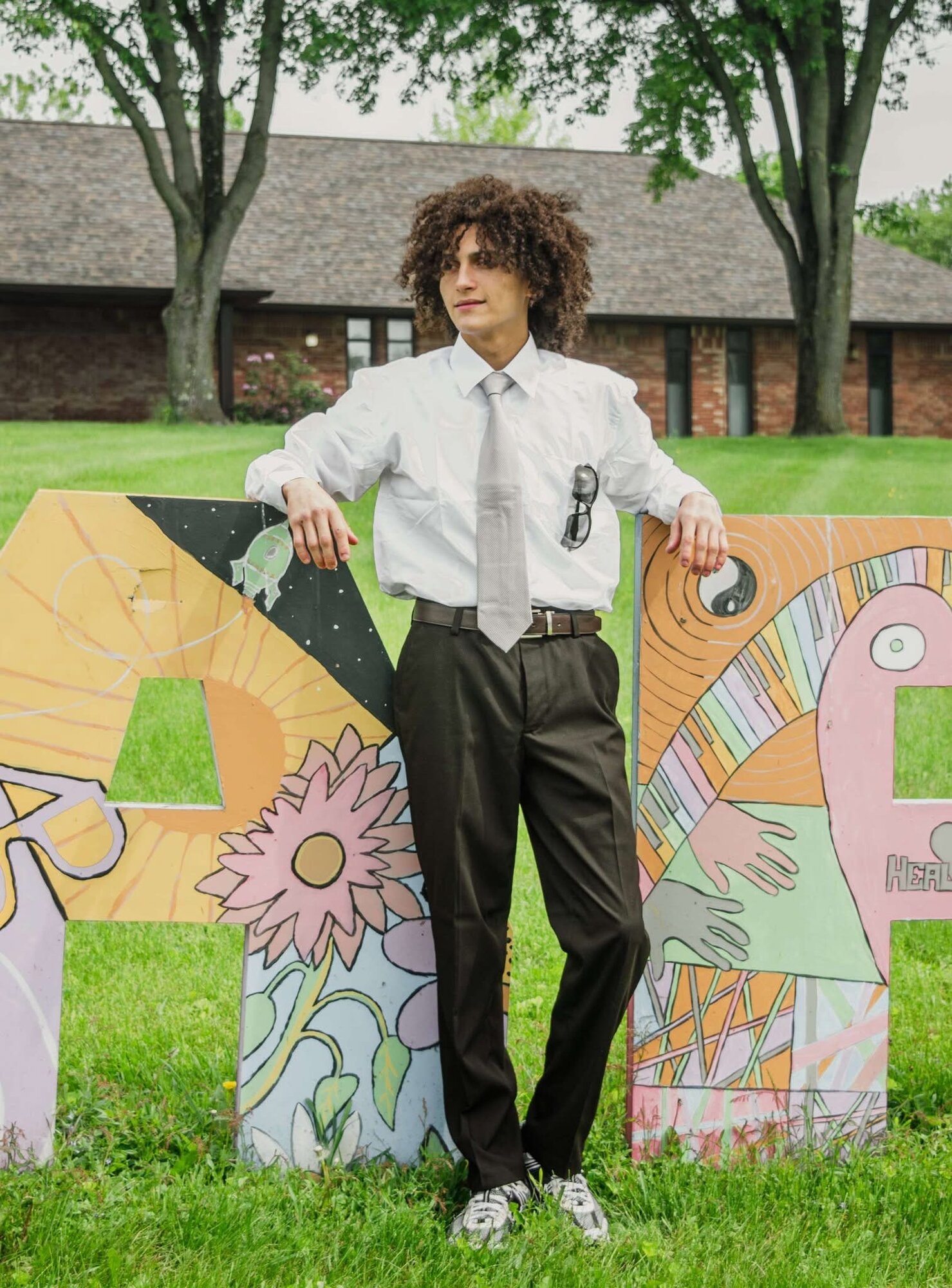 Senior portrait of an adult in shirt and tie posed with painted letter art on a lawn