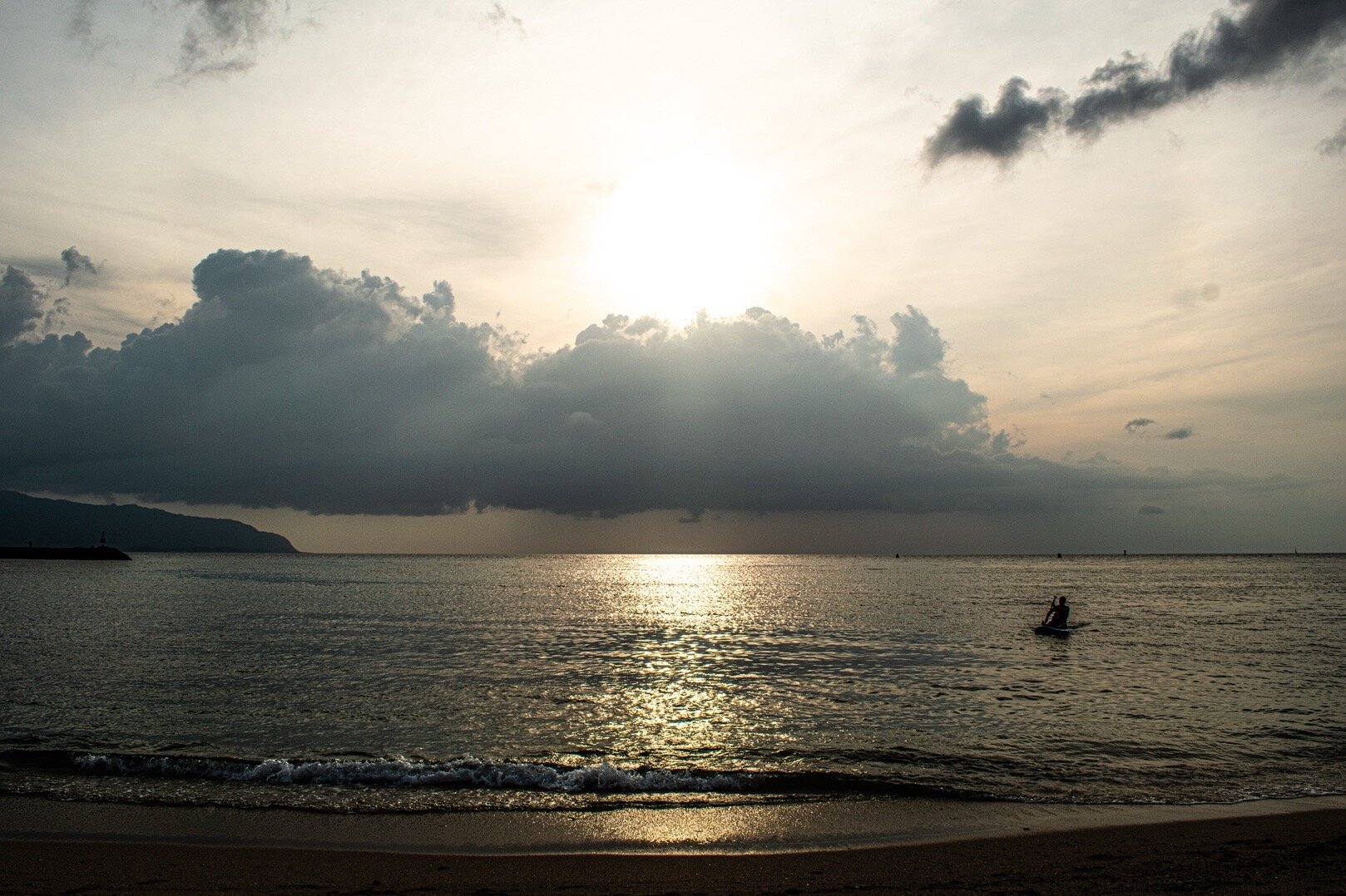 Swimmer in calm ocean water at sunset with golden clouds