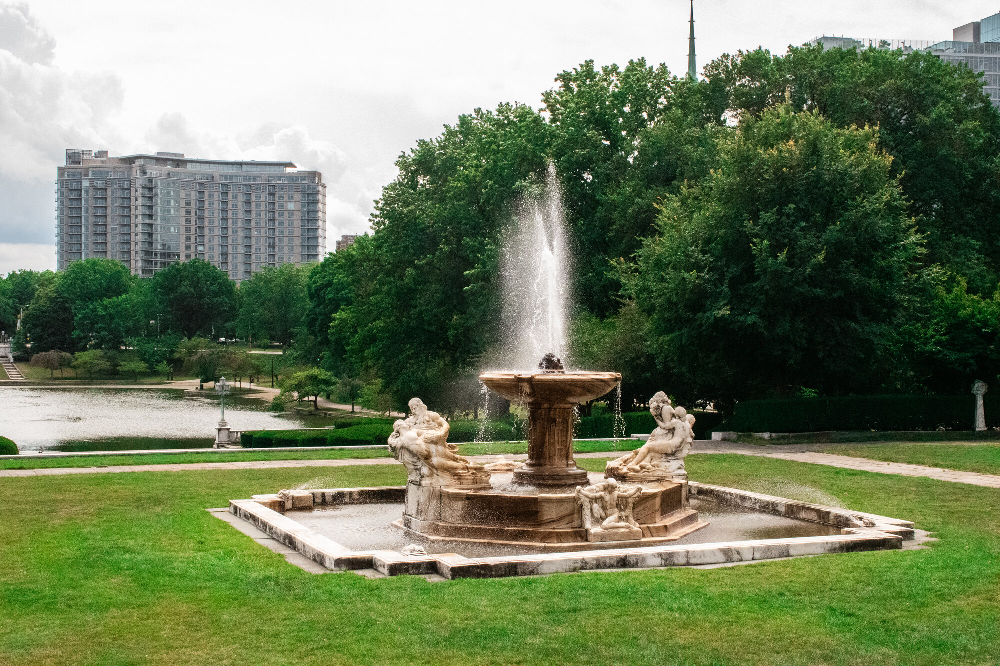 Classical sculpted fountain in a formal garden with a lagoon and city skyline beyond
