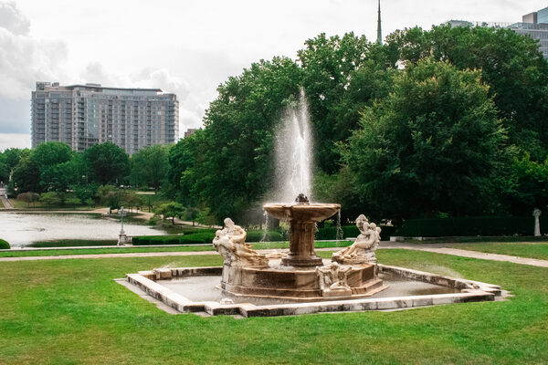Classical sculpted fountain in a formal garden with a lagoon and city skyline beyond