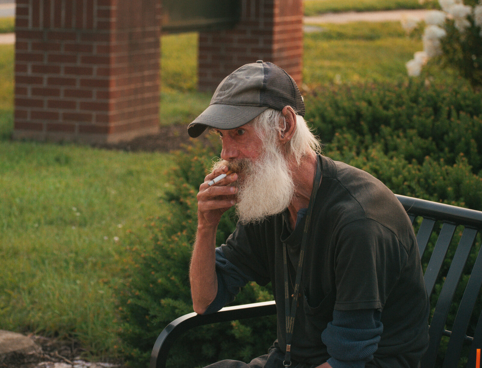Candid documentary portrait of a bearded man smoking on a park bench in warm evening light