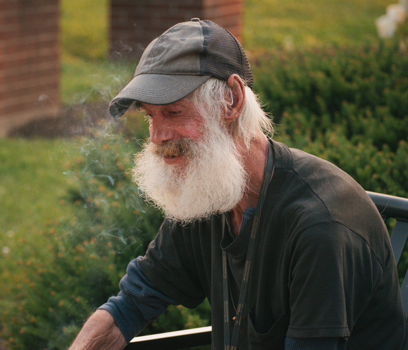 Close documentary portrait of a bearded man smiling through drifting smoke at golden hour