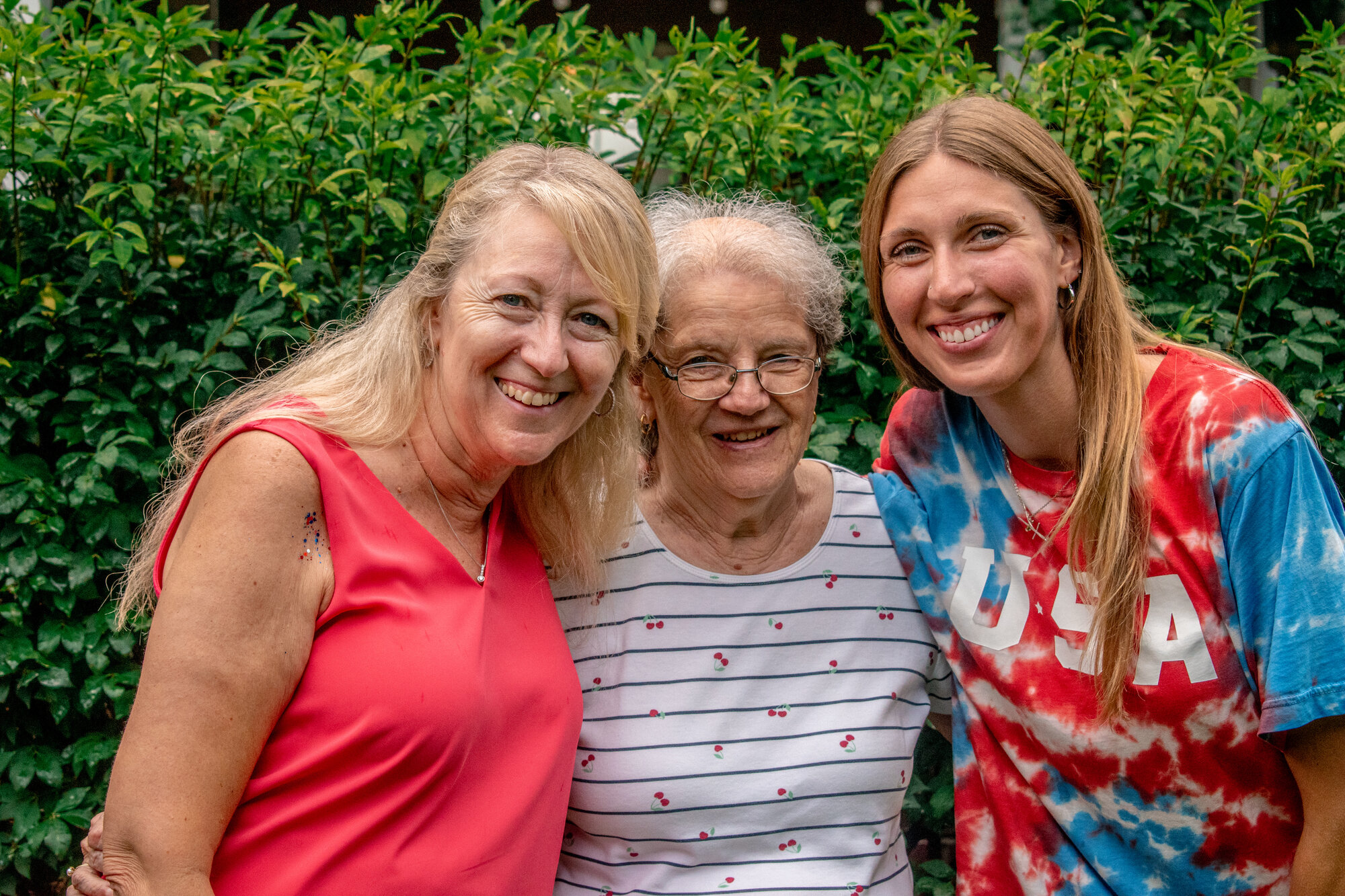 Three adult women smiling together at an outdoor summer gathering