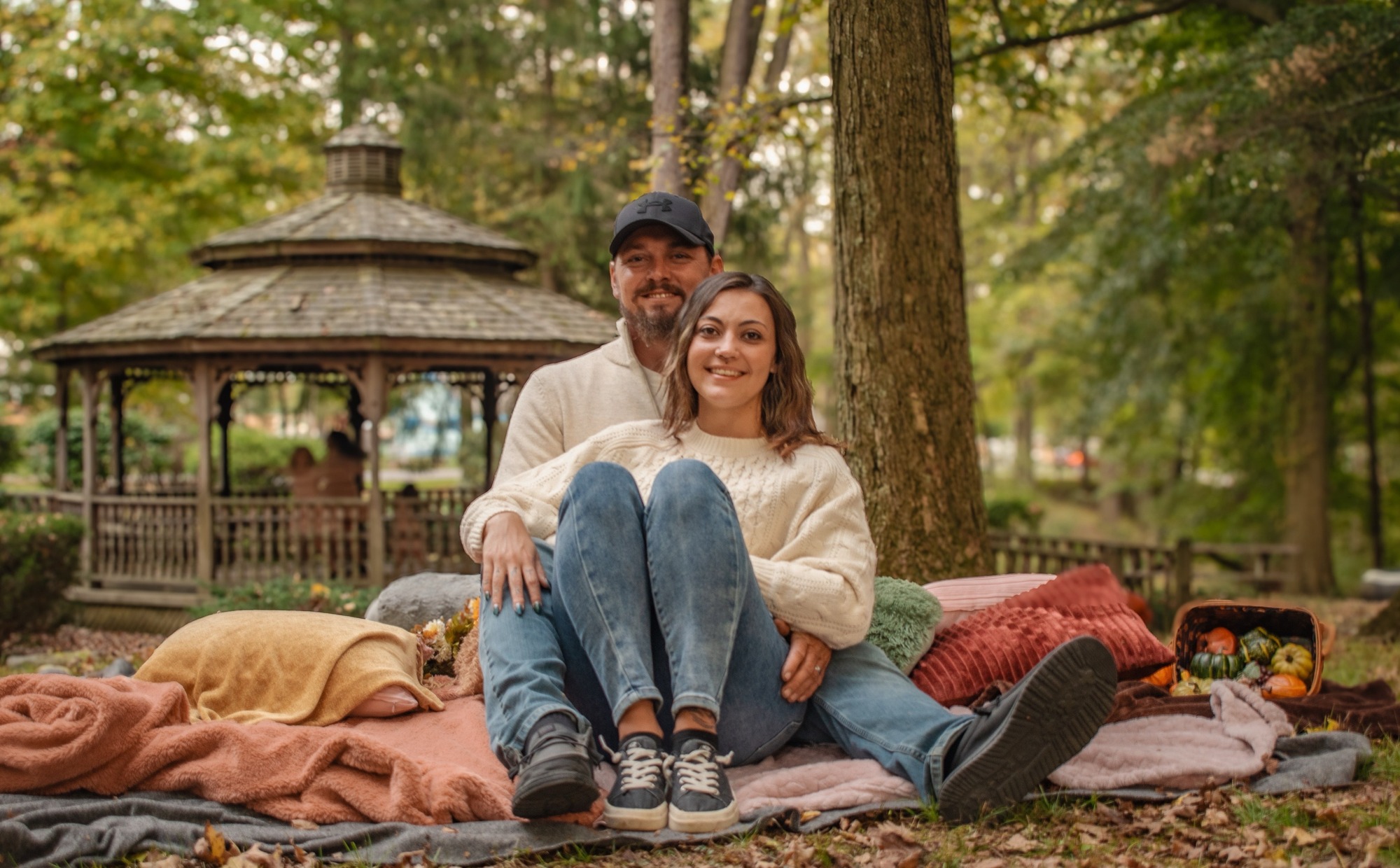 Couple sitting together on blanket in autumn park with gazebo behind