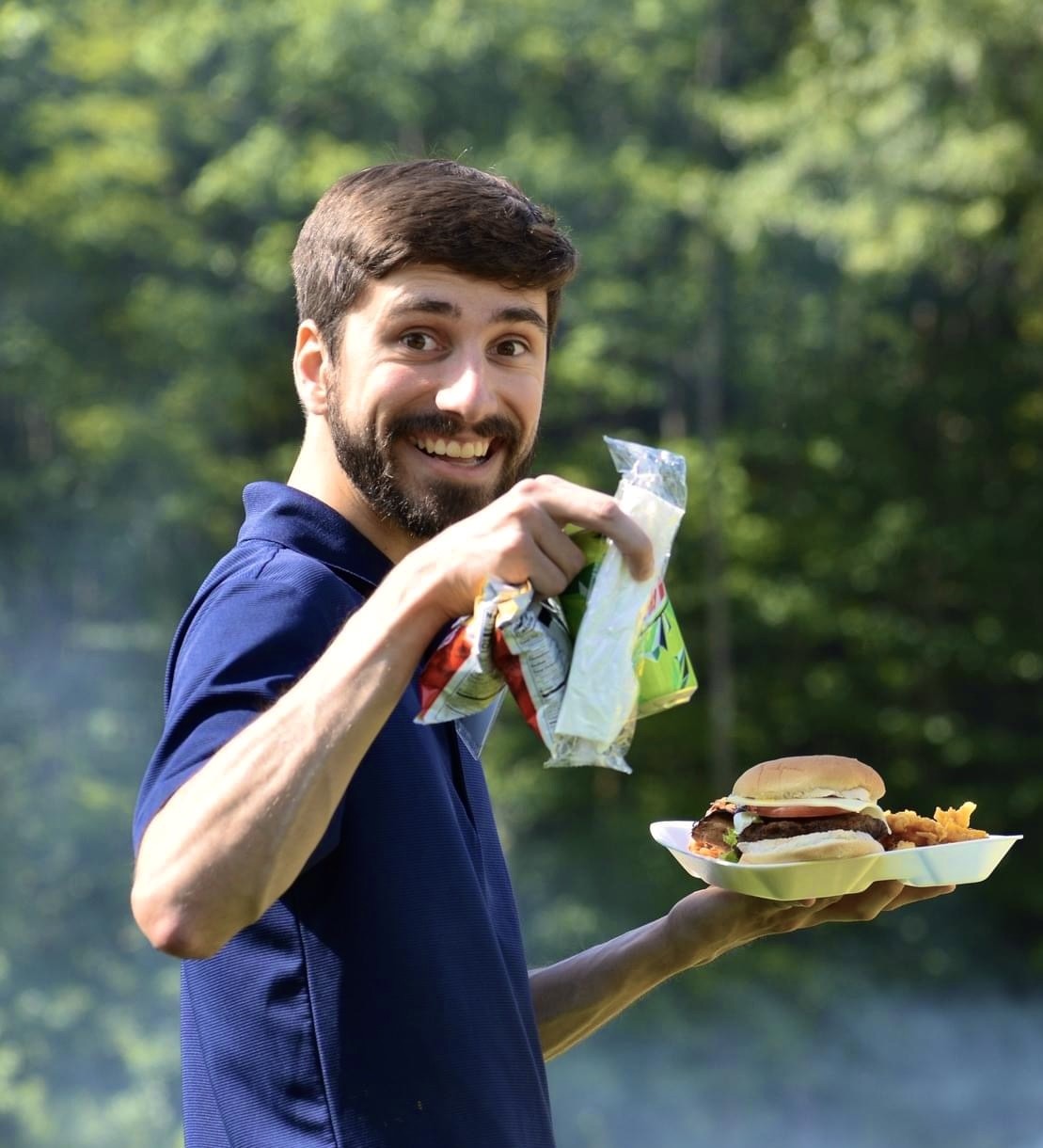 Candid portrait of a smiling man holding a plate of picnic food at an outdoor gathering