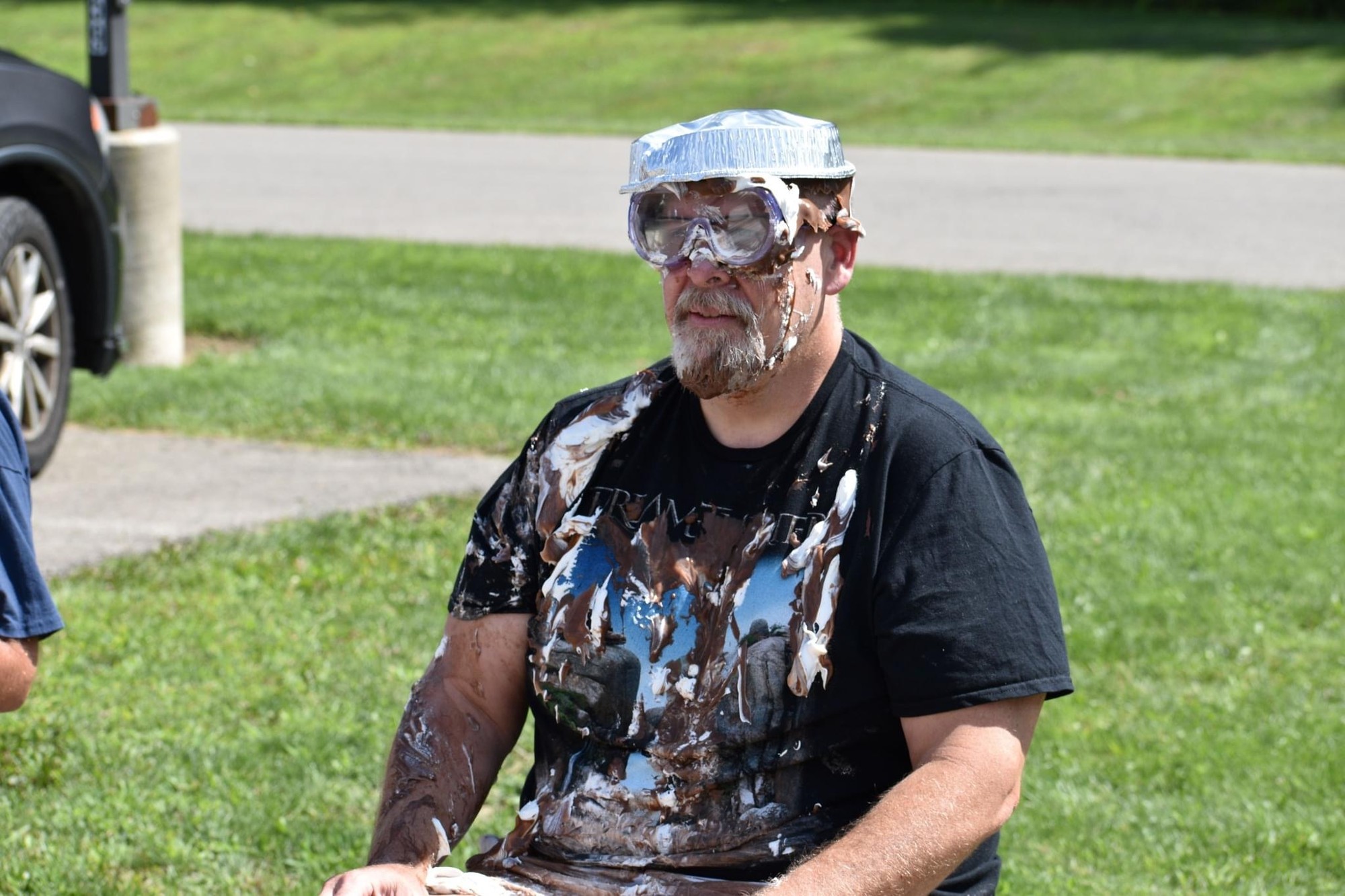 Adult participant wearing goggles and a foil pie tin on his head after an outdoor pie event