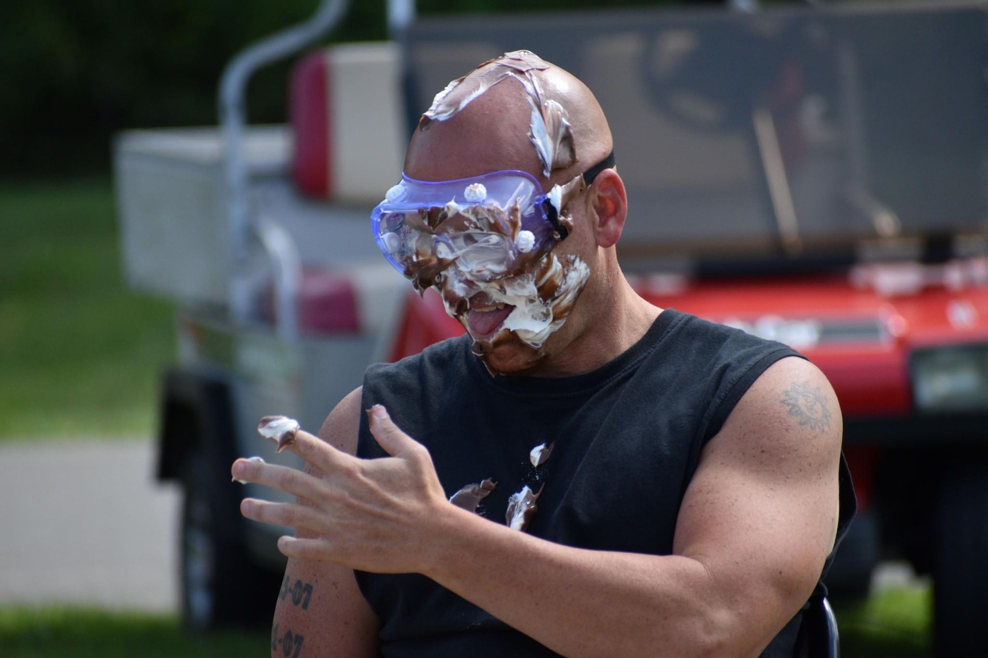 Candid moment of an adult wearing goggles and covered in cream during an outdoor pie event