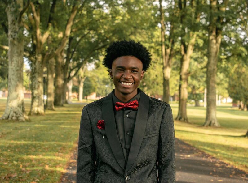 Senior portrait of an adult in a black suit with red bow tie among autumn trees
