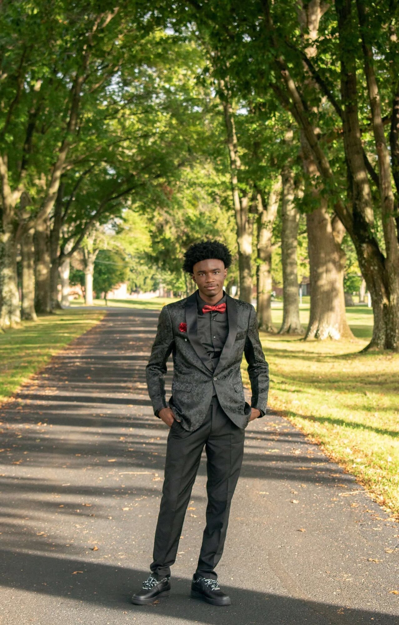 Full-length senior portrait of an adult on a tree-lined path in evening light