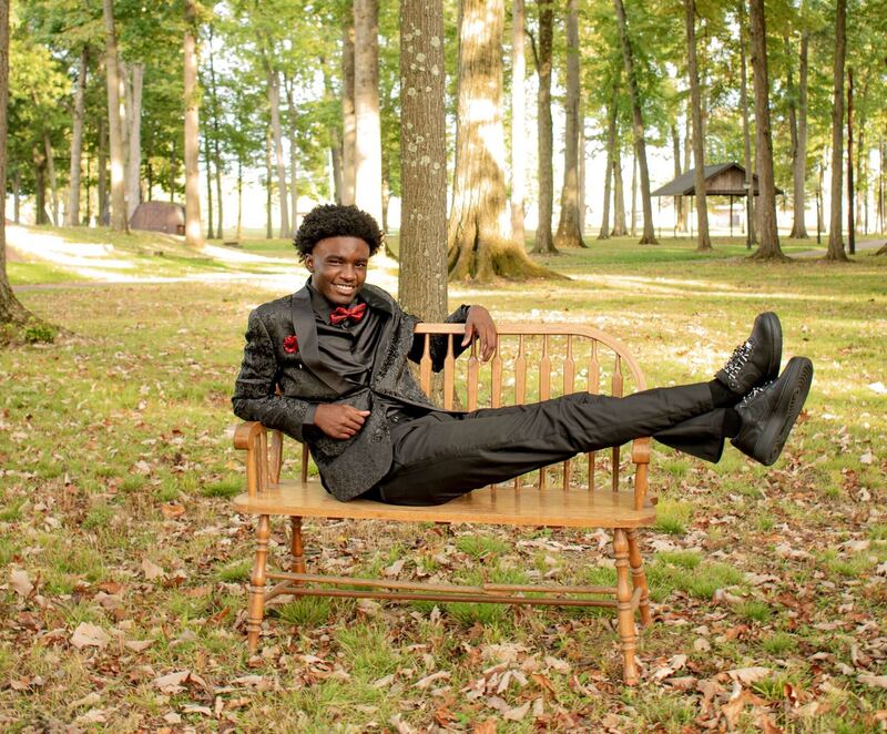 Relaxed senior portrait of an adult seated on a wooden bench in a forest clearing