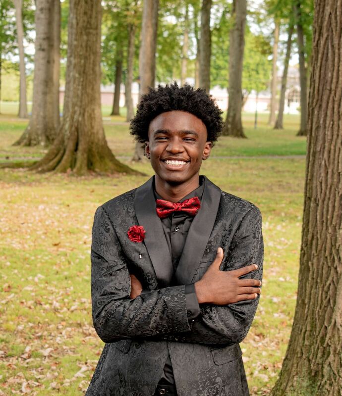 Confident senior portrait of an adult with arms crossed among tall trees