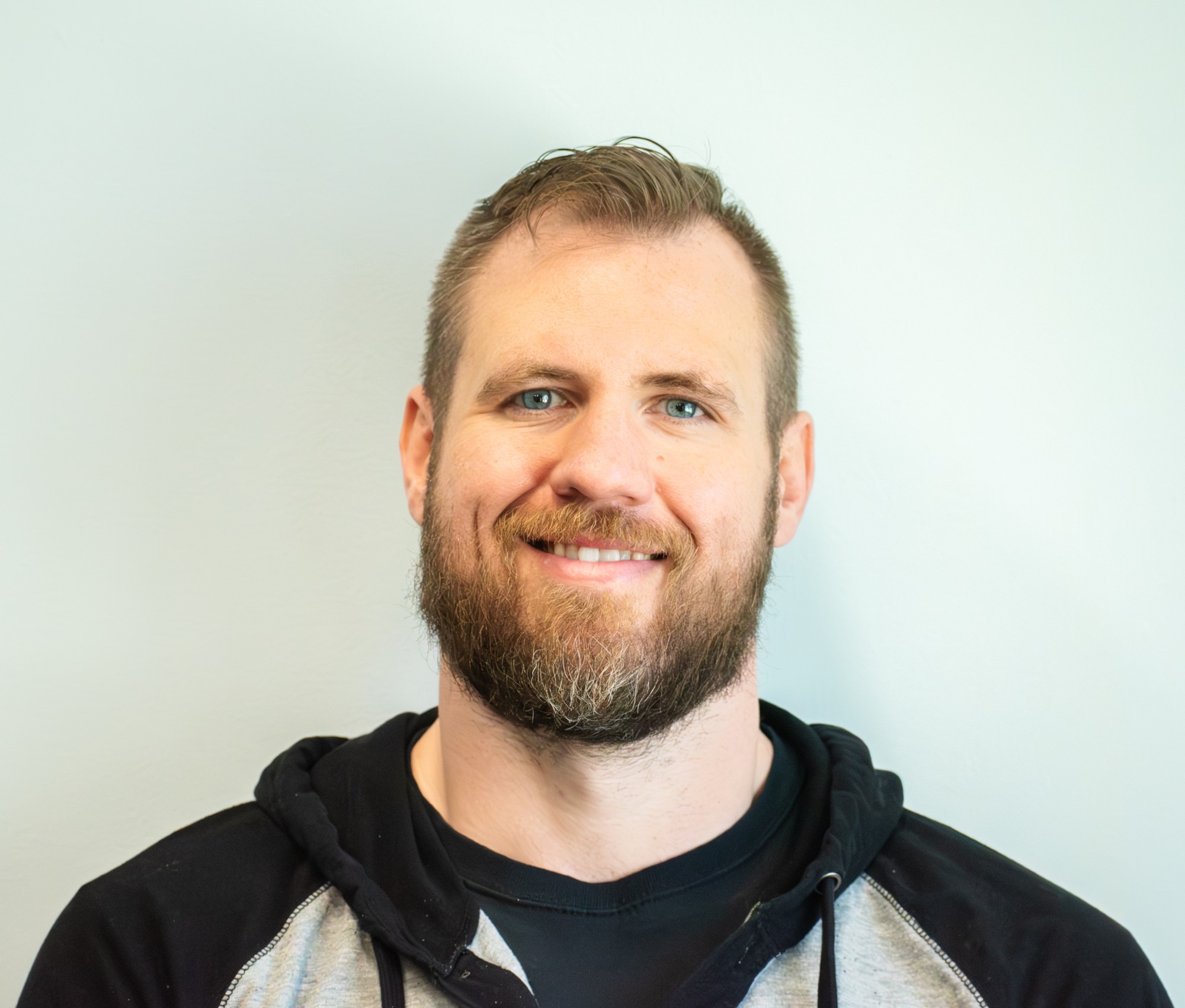 Indoor headshot of a smiling bearded man against a soft pale background