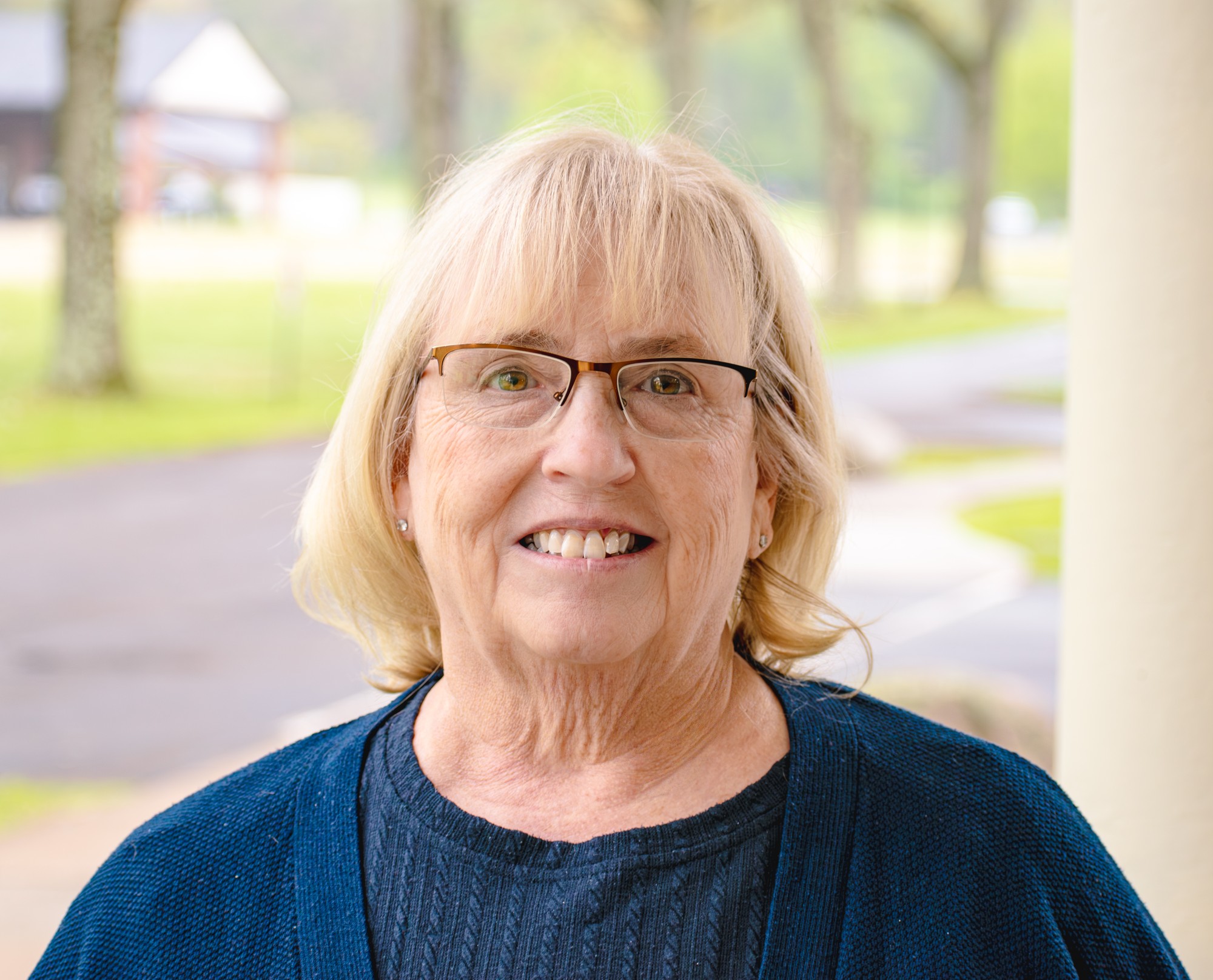 Outdoor headshot of a smiling woman in glasses and a navy cardigan