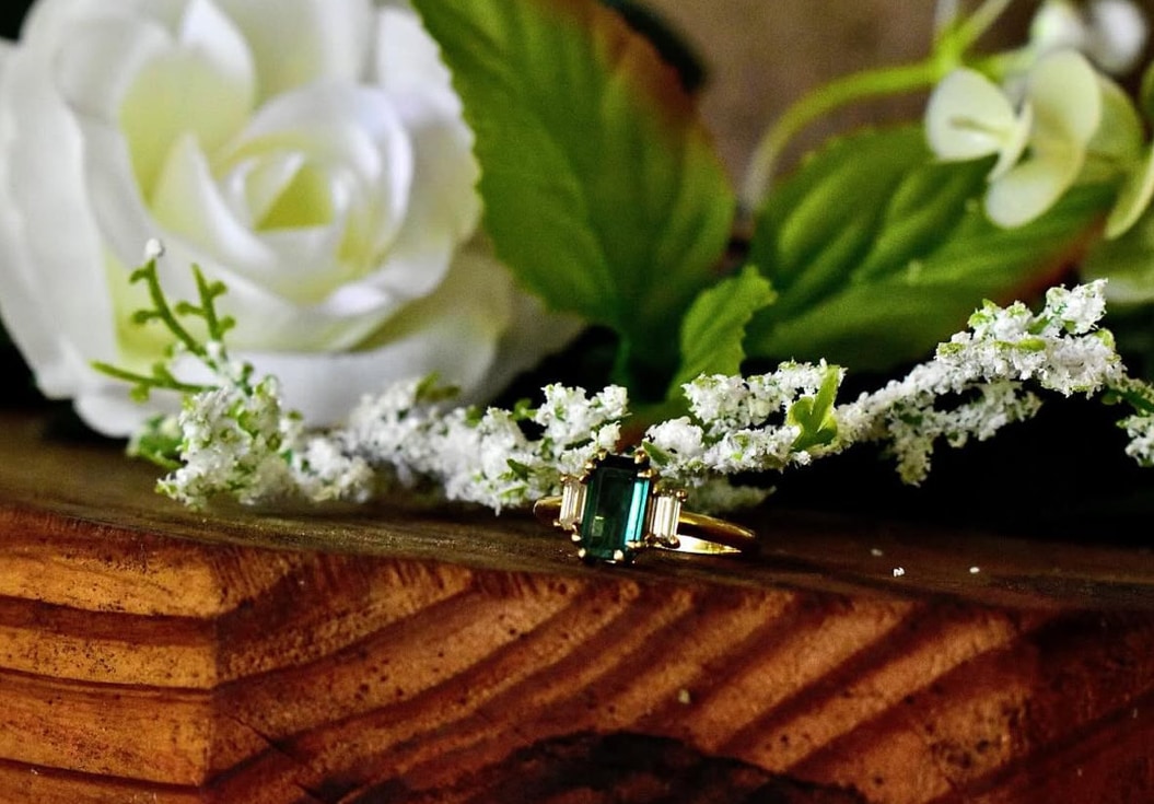 Emerald-cut green gemstone ring styled with white wedding florals on richly grained wood