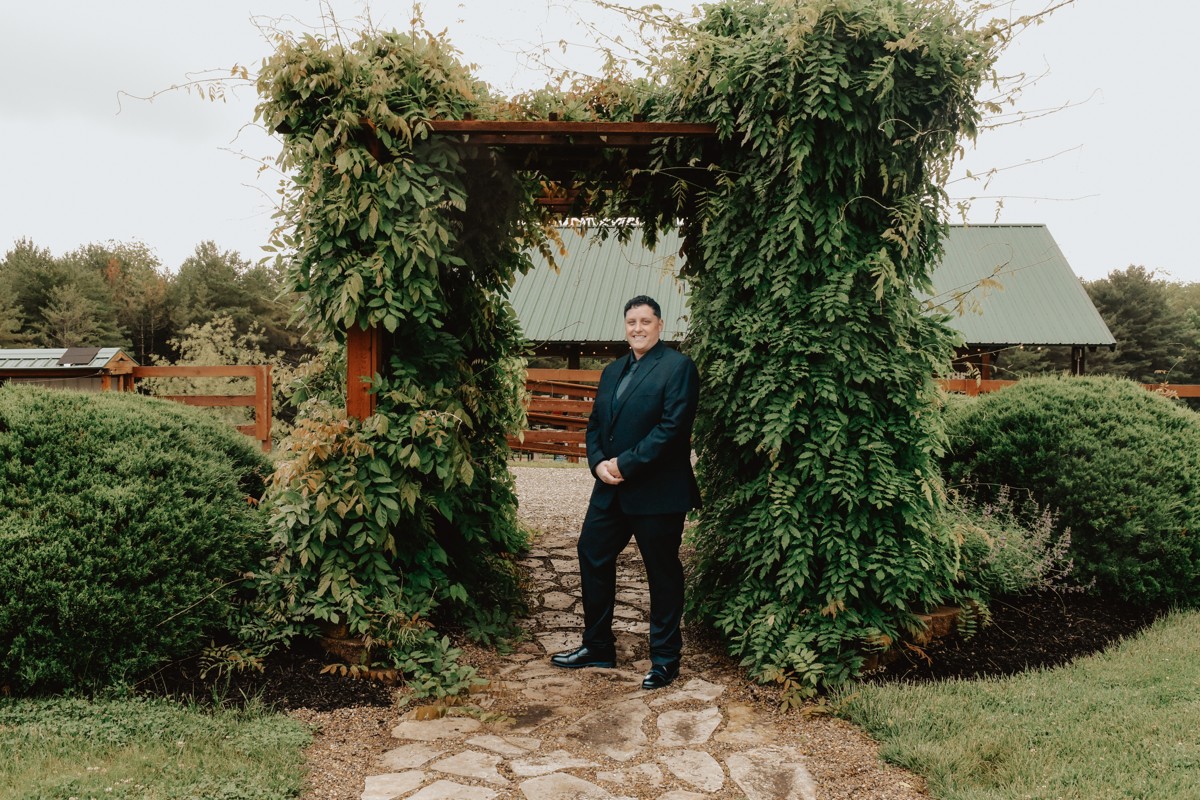 Wedding portrait in a dark suit beneath a lush vine-covered garden arbor
