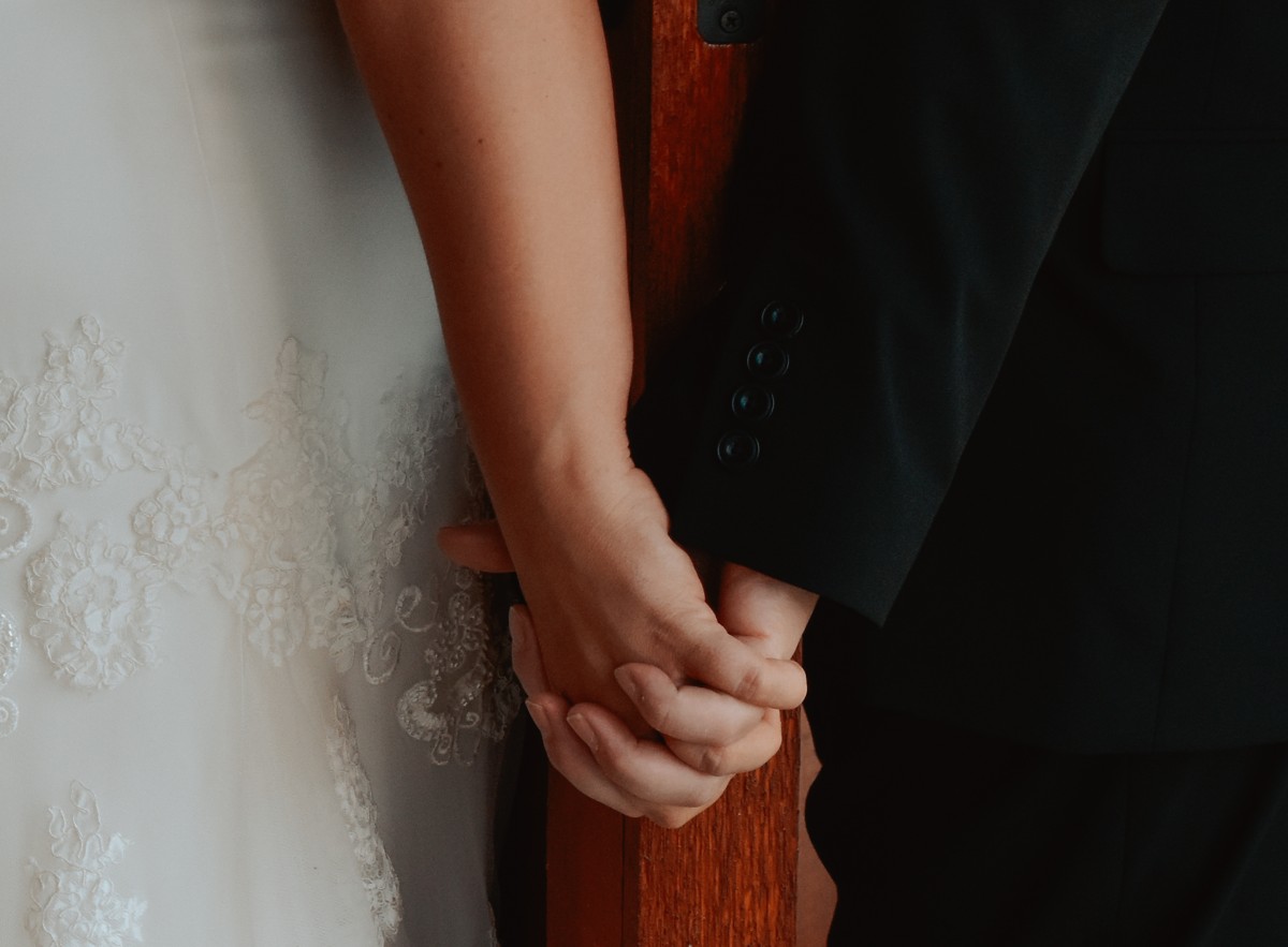 Close-up of the couple holding hands around a wooden doorway before the ceremony