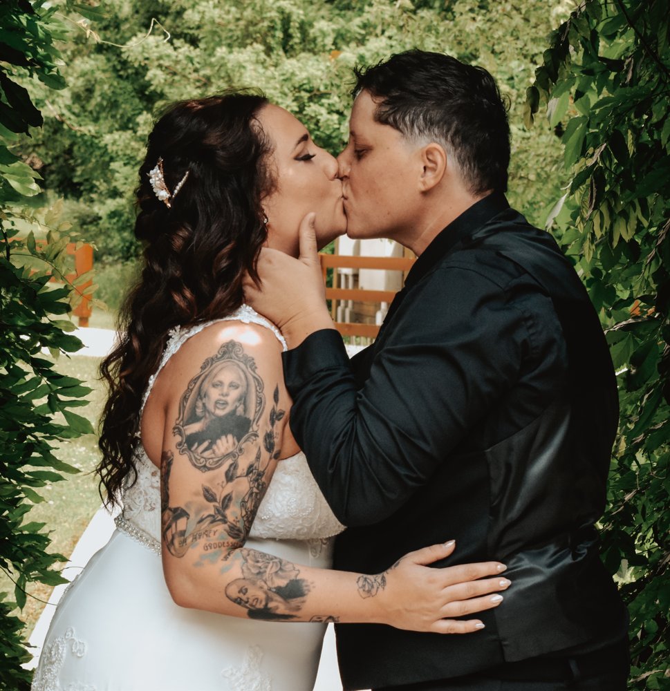 Newlyweds kissing beneath leafy branches