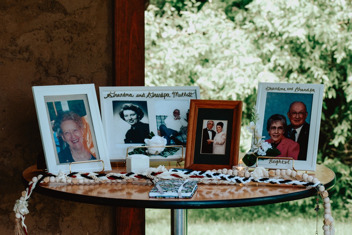 Wedding remembrance table with framed family photographs, flowers, and candles beside a window