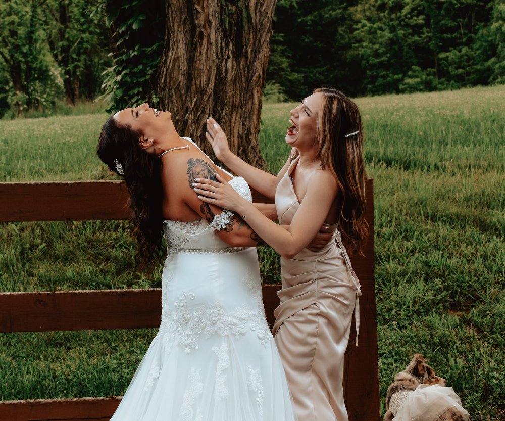 Bride laughing with a guest in a champagne dress beside a wooden fence