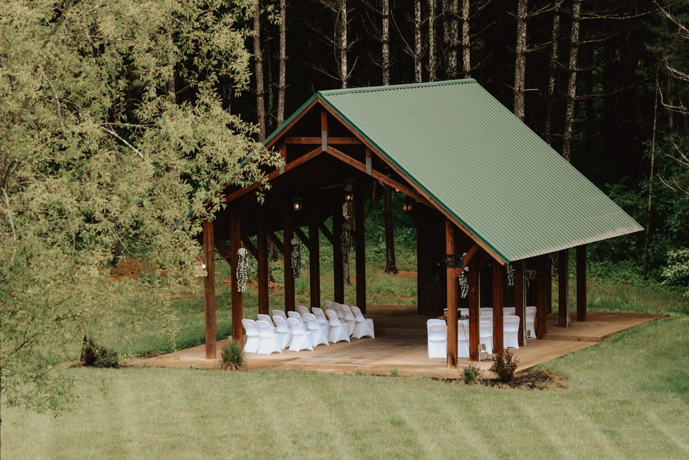 Woodland ceremony pavilion with a green roof and rows of white chairs