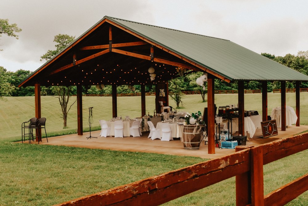 Reception pavilion with white chairs and tables viewed across a wooden fence