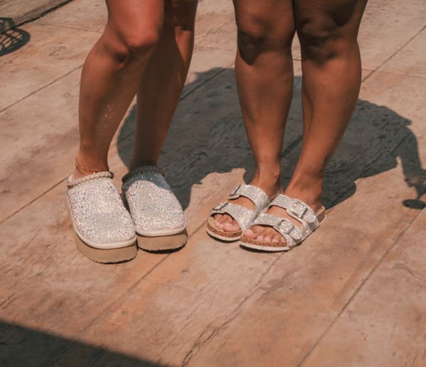 Detail of the couple's sparkling and silver sandals side by side on a wooden deck
