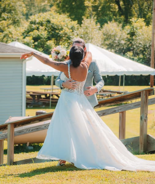 Bride twirling in her gown, bouquet raised, in front of the reception tent