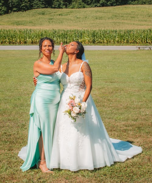 Playful moment between the bride and a bridesmaid in a mint gown on the lawn