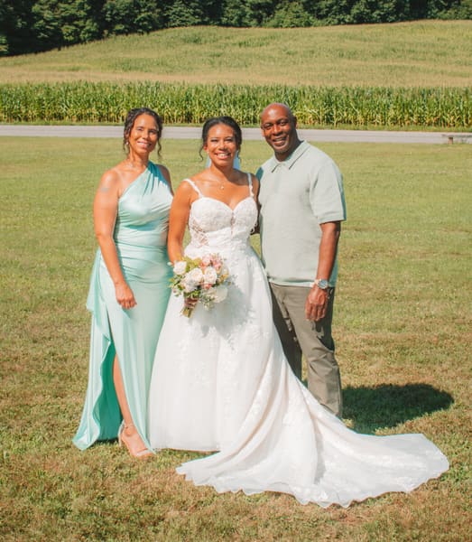 Bride holding her bouquet posing with two family members on a sunny field
