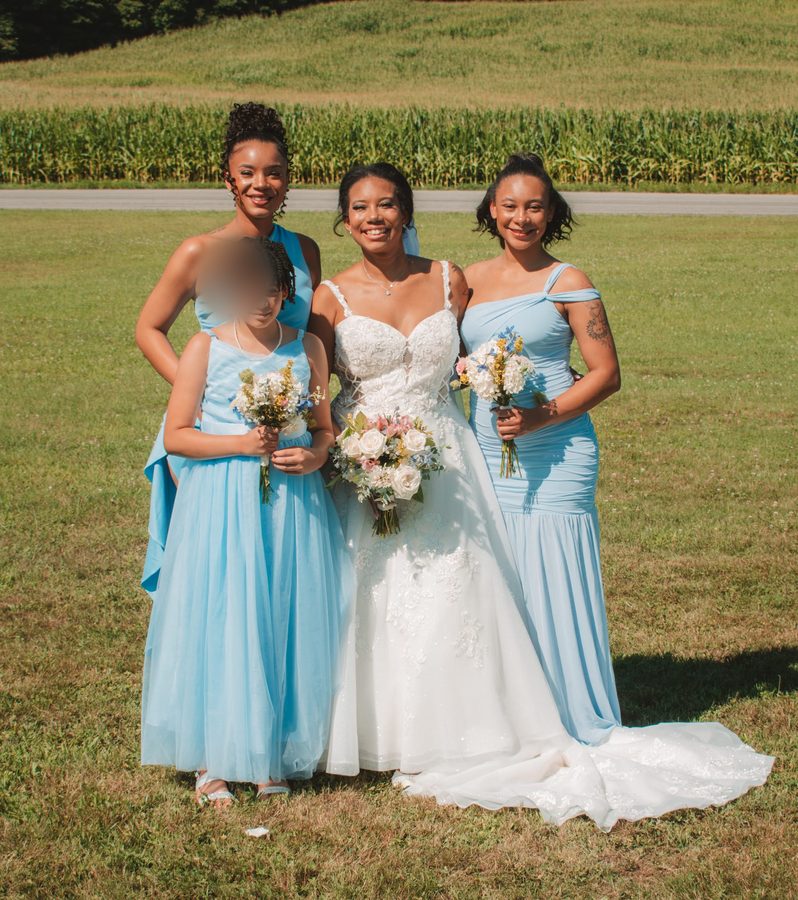 Bride with wedding attendants in dusty blue dresses, with a minor's face blurred for privacy