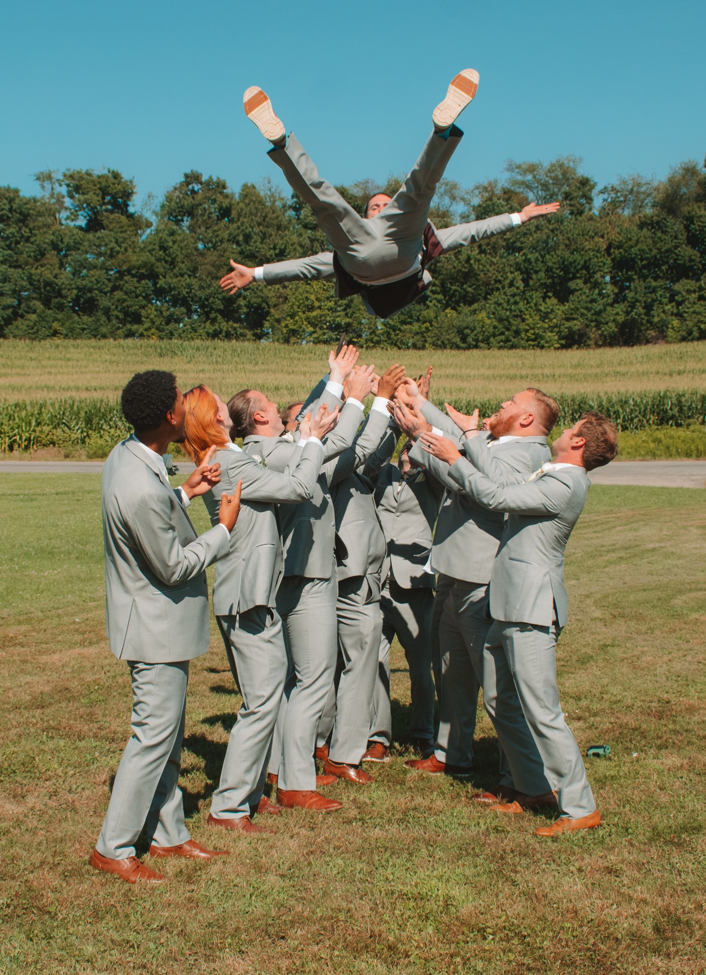Chet being tossed into the air by his groomsmen beneath a clear blue August sky