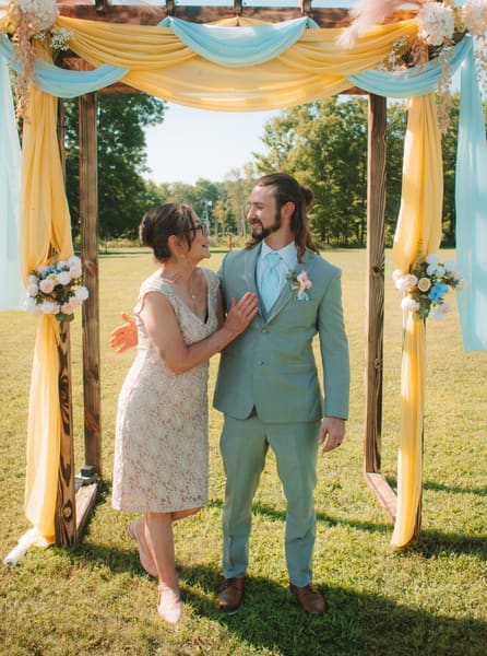 Bride and groom smiling at each other beneath a yellow-and-blue draped ceremony arbor