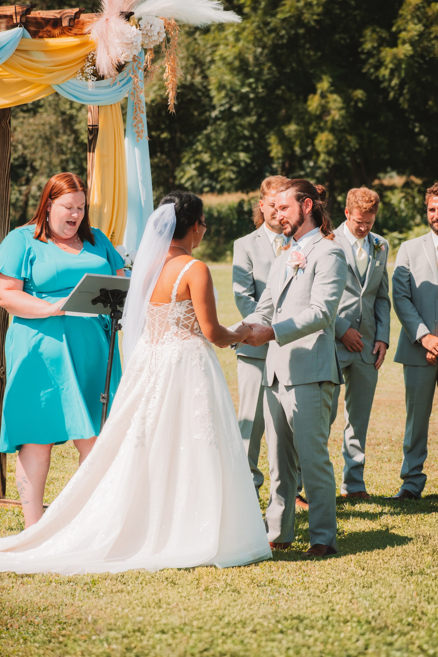 Newlyweds exchanging vows while adult members of their wedding party look on