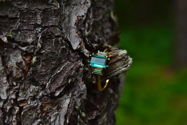 Emerald-cut green gemstone ring tucked into textured tree bark