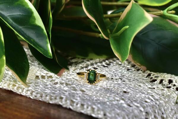 Gold emerald-cut ring styled on lace with glossy magnolia leaves
