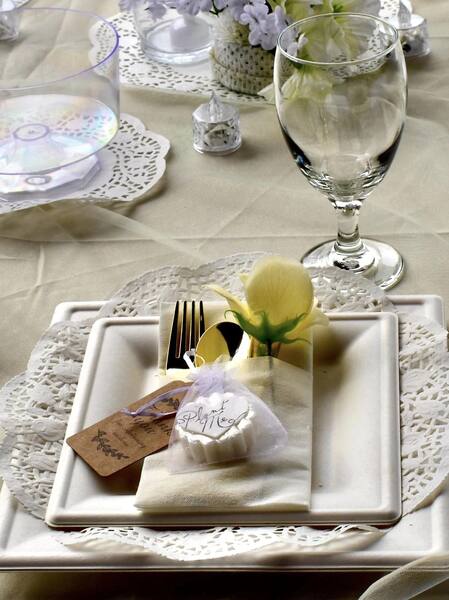 Elegant wedding place setting with a lace-edged plate, glassware, and plantable favor