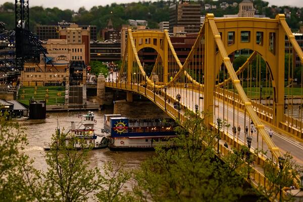 Yellow Pittsburgh bridge over river with riverboat and city skyline behind